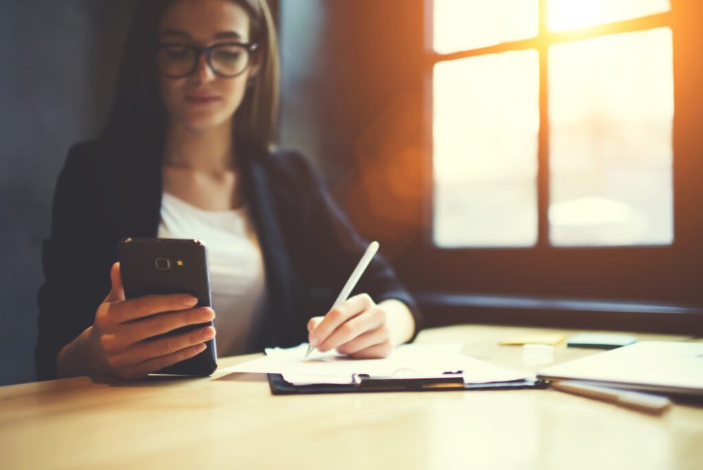 Selective focus on skilled female marketing expert holding smartphone dialing number of customer while using creative ideas for campaign, student preparing to examination and sharing files online