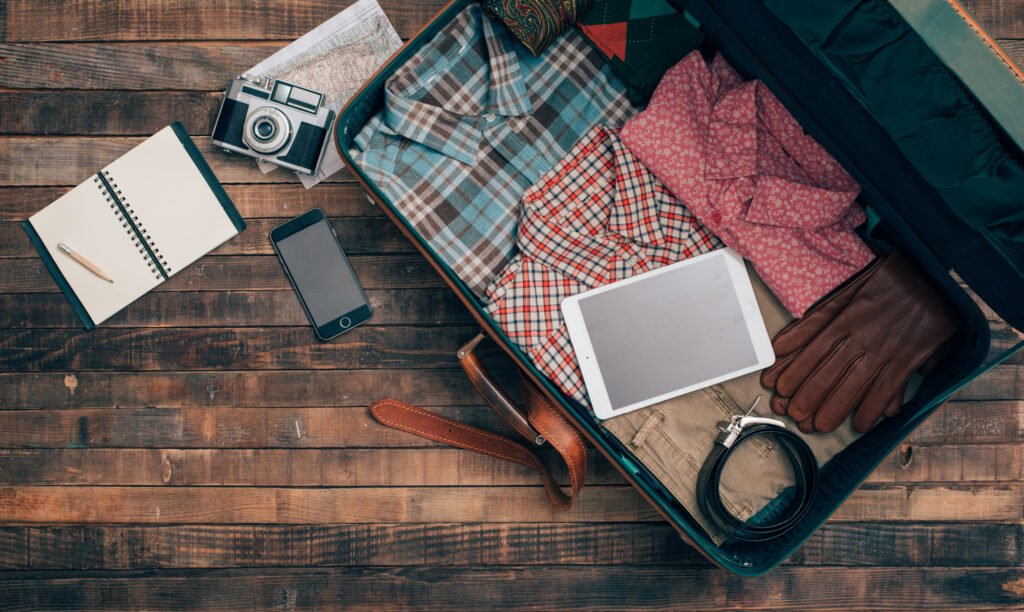 Vintage hipster traveler packing, open suitcase on a wooden table with clothing, camera and mobile phone, top view