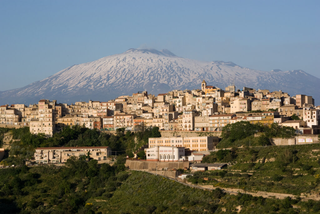 view of dwellings and belltower in the city of Centuripe in Sicily, on background the volcano Etna partly snowy