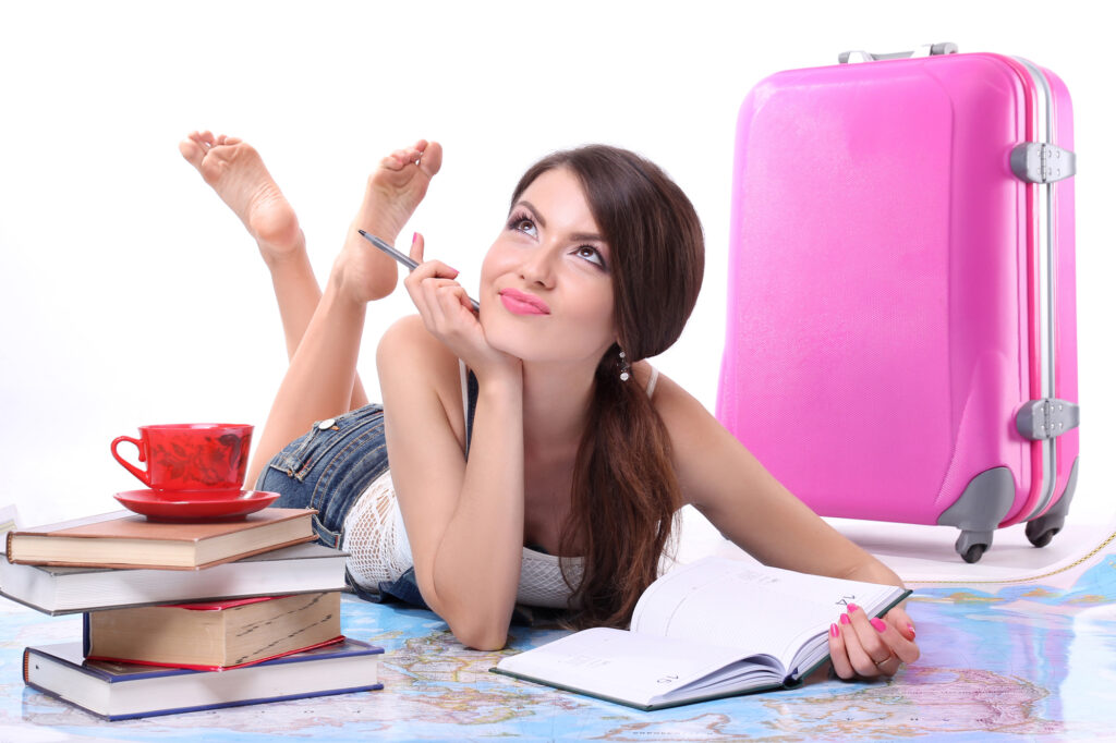 Young happy woman with a suitcase lying on the plan maps trips. Concept vacation.